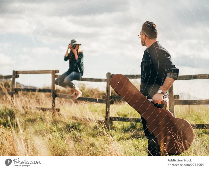 Frau, die mit der Gitarre einen Mann fotografiert. Natur Musiker Fotograf fallen sitzen ländlich Zaun Lifestyle Mensch Sommer lässig akustisch gutaussehend Typ