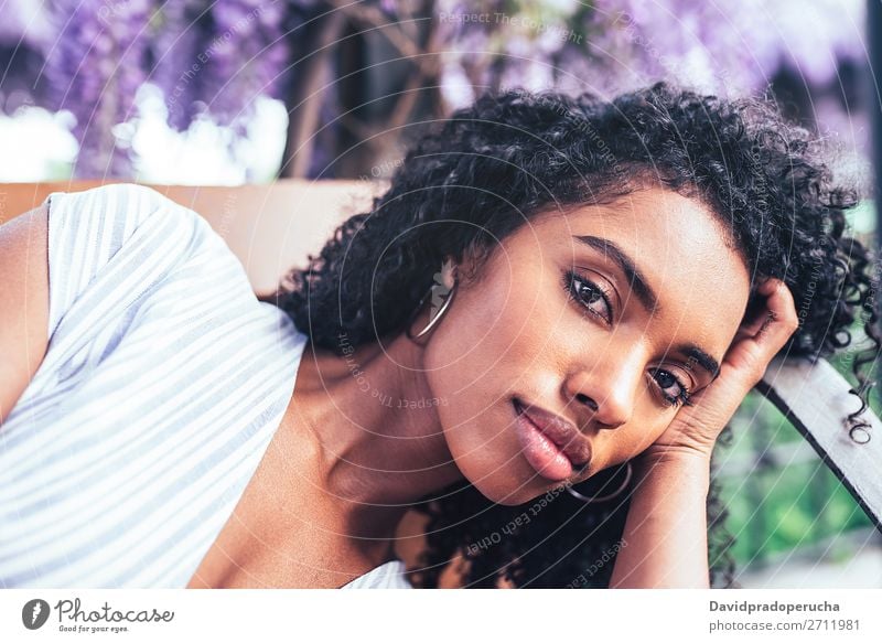 Junge schwarze Frau, die sich auf einen Stuhl legt, umgeben von Blumen. Blüte Frühling Fliederbusch Porträt multiethnisch Afrikanisch