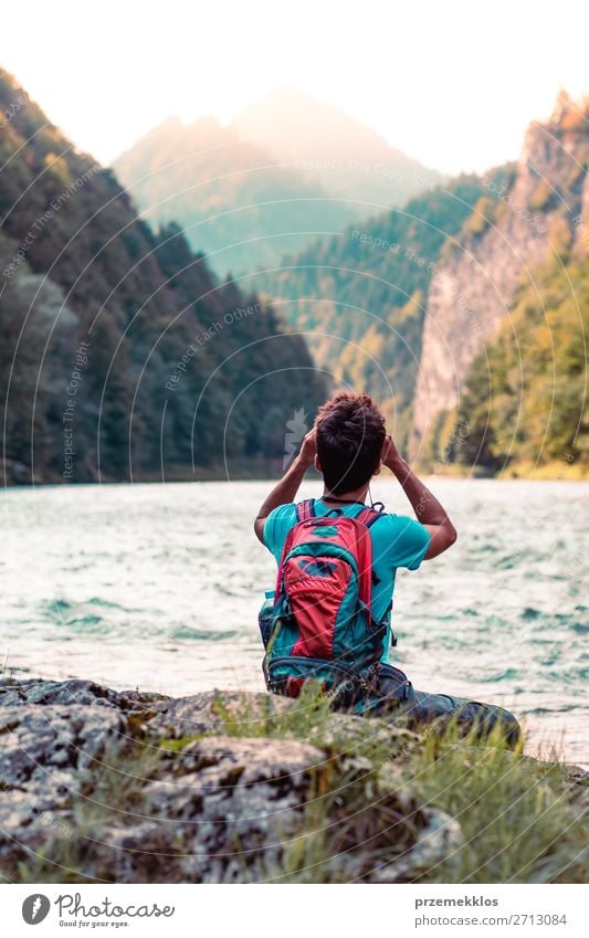 Junger Tourist mit Rucksack schaut durch ein Fernglas. Lifestyle Leben Freizeit & Hobby Ferien & Urlaub & Reisen Ausflug Sommer Berge u. Gebirge Mensch