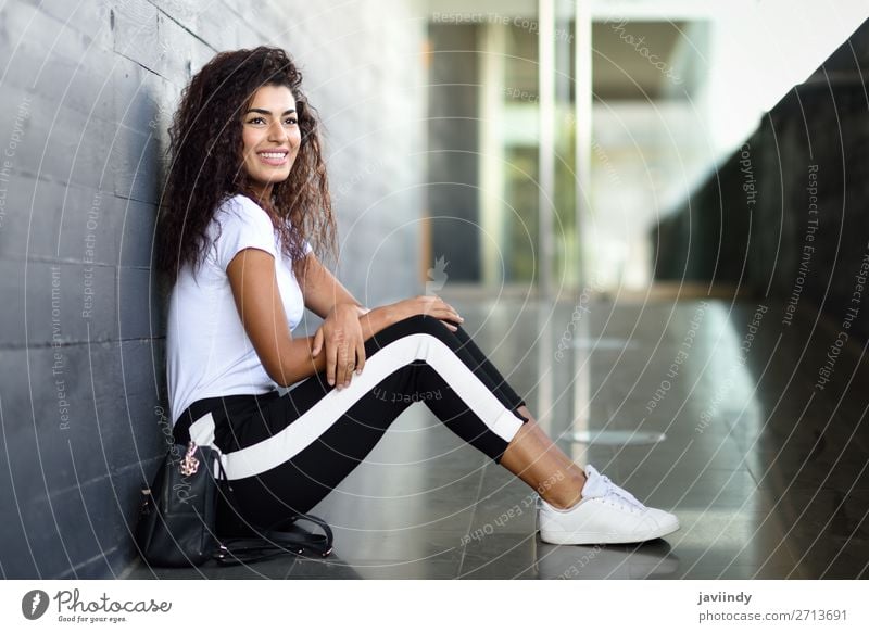 Afrikanische Frau mit schwarzer lockiger Frisur, die auf dem Stadtboden sitzt. Lifestyle Stil Glück schön Haare & Frisuren Gesicht Sport Mensch feminin