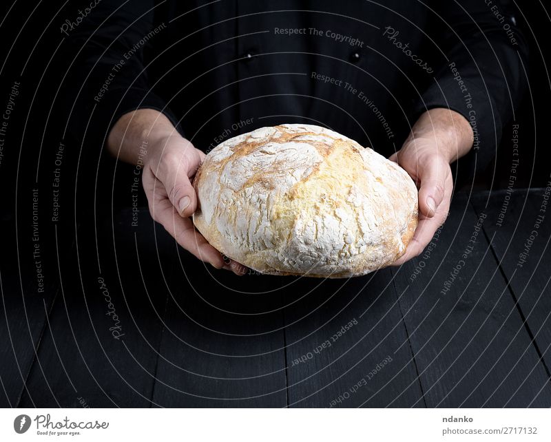 männliche Kochhände halten einen ganzen Laib gebackenes Rundbrot. Brot Ernährung Tisch Küche Mensch Mann Erwachsene Hand Holz machen dunkel frisch braun schwarz