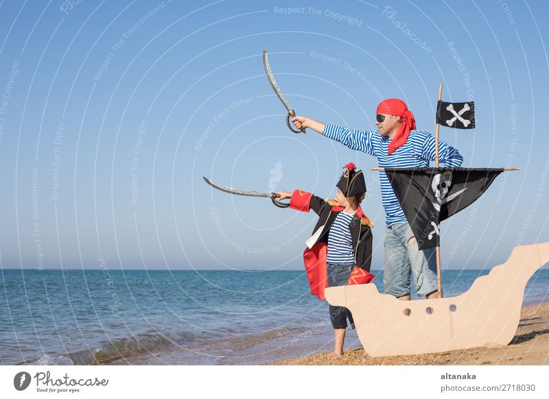 Vater und Sohn spielen zur Tageszeit am Strand. Sie sind mit Matrosenwesten und Piratenkostümen bekleidet. Konzept des glücklichen Spiels im Urlaub und der freundlichen Familie.