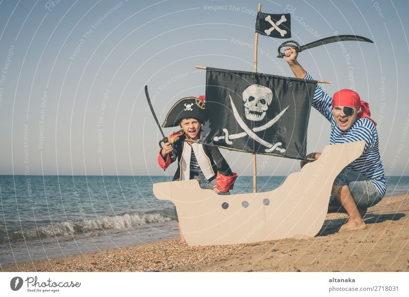 Vater und Sohn spielen zur Tageszeit am Strand. Sie sind mit Matrosenwesten und Piratenkostümen bekleidet. Konzept des glücklichen Spiels im Urlaub und der freundlichen Familie.