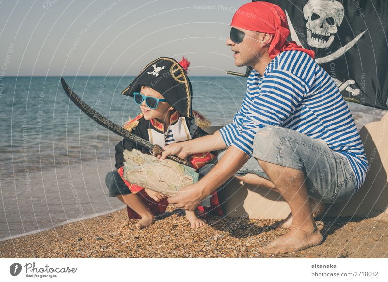 Vater und Sohn spielen zur Tageszeit am Strand. Sie sind mit Matrosenwesten und Piratenkostümen bekleidet. Konzept des glücklichen Spiels im Urlaub und der freundlichen Familie.