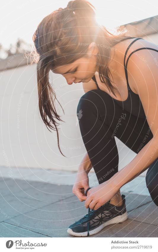 Sportliche Frau mit Schnürsenkeln an Sneakers sportlich hübsch Kopplungsbindung Straffung Schuhe Turnschuh Jugendliche heiter Park Großstadt schön Lifestyle