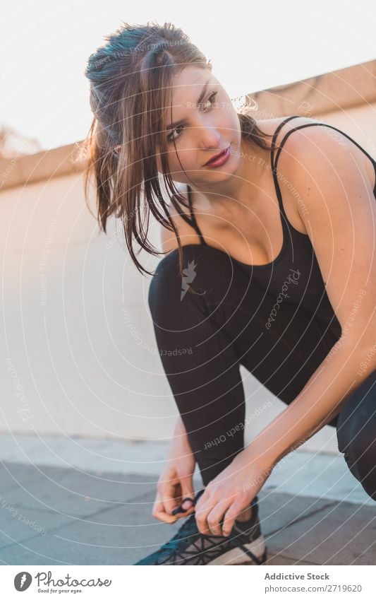 Sportliche Frau mit Schnürsenkeln an Sneakers sportlich hübsch Kopplungsbindung Straffung Schuhe Turnschuh Jugendliche heiter Park Großstadt schön Lifestyle