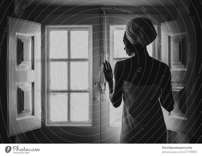 Eine Frau, die in ein Handtuch gehüllt ist und durch ein altes Fenster schaut. schwarz Erwachsene Hintergrundbild Beautyfotografie attraktiv Fürsorge urwüchsig