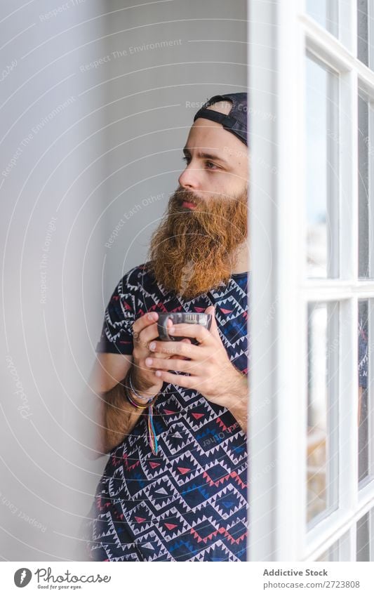 Bartiger Mann mit Becher heimwärts Erholung Erwachsene bärtig stehen Tasse heiß trinken Fenster lässig Jugendliche Haus Lifestyle Raum gutaussehend Leben Glück