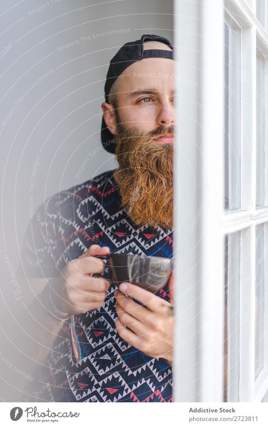 Bartiger Mann mit Becher heimwärts Erholung Erwachsene bärtig stehen Tasse heiß trinken Fenster lässig Jugendliche Haus Lifestyle Raum gutaussehend Leben Glück