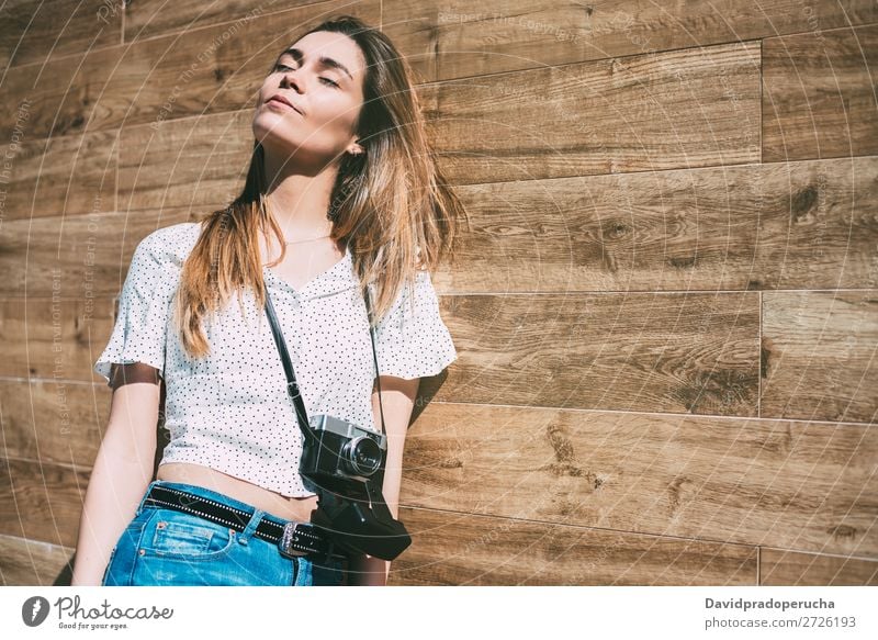 Schöne Frau mit alter Kamera, die an einer Holzwand steht. altehrwürdig Fotokamera retro Jugendliche schön Rolle Porträt Fotografie vereinzelt Beautyfotografie