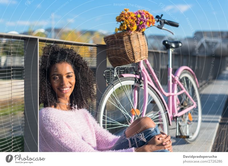 Schwarze junge Frau sitzt mit ihrem alten Fahrrad am Fluss. Mädchen schön retro Blume Glück altehrwürdig Blumenstrauß rosa Sommer Jugendliche hübsch Frühling