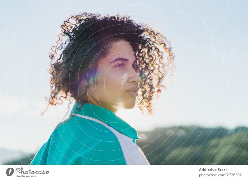 Lockenförmige Frau, die im Sonnenlicht auf der Natur posiert. Sommer genießen Körperhaltung Menschliches Gesicht Landschaft Farbe Porträt lockig ruhig