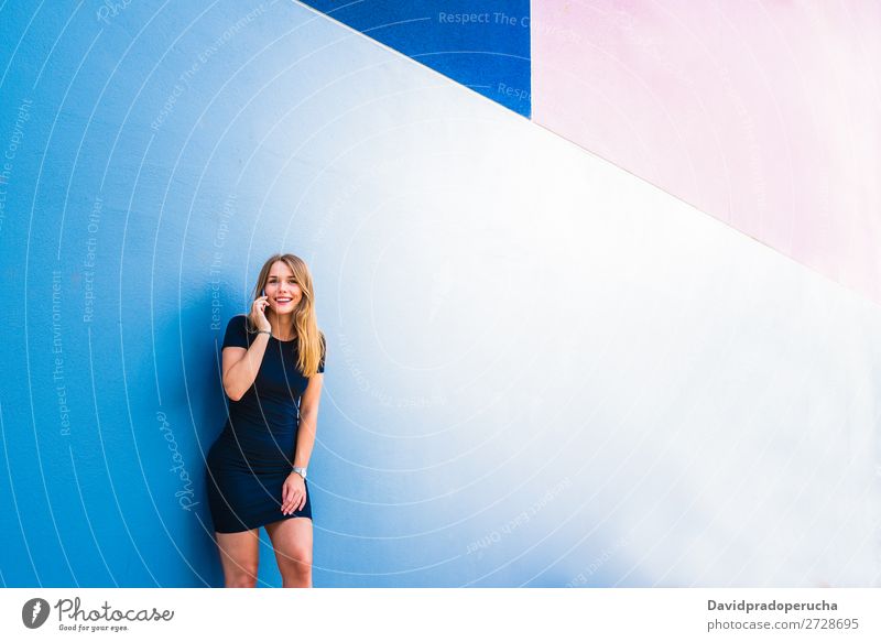 Glückliche junge Frau auf dem Handy an einer bunten Wand mehrfarbig blond Telefon Mobile Technik & Technologie Kleid Außenaufnahme Jugendliche Beautyfotografie