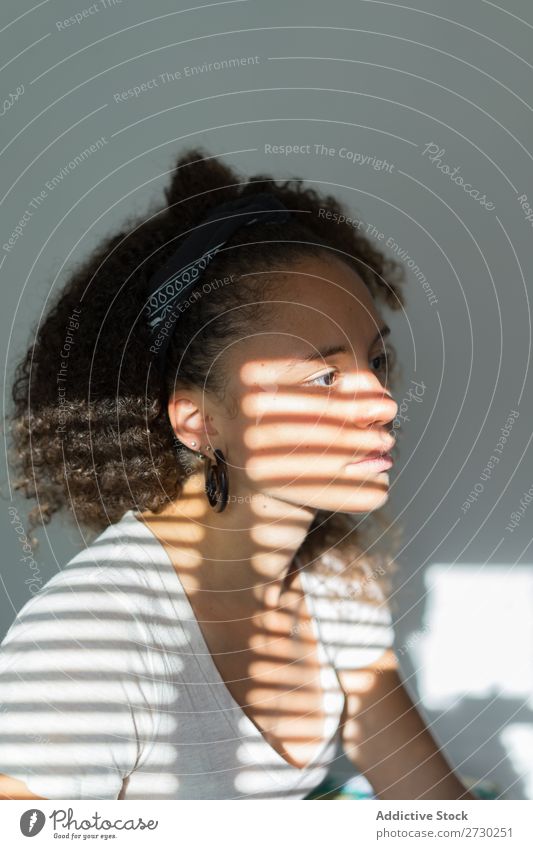 Frau, die im Schatten von Jalousien posiert. Fenster Hochsitz feminin Sonnenlicht Menschliches Gesicht Porträt Innenarchitektur Muster gestreift Wohnung Licht