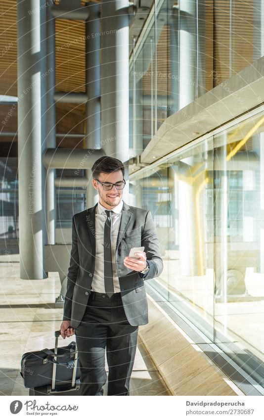 junger Geschäftsmann, der mit seinem Handy am Flughafen spazieren geht. Mobile Telefon Technik & Technologie laufen Mitteilung Lächeln Fenster Abflughalle Anzug