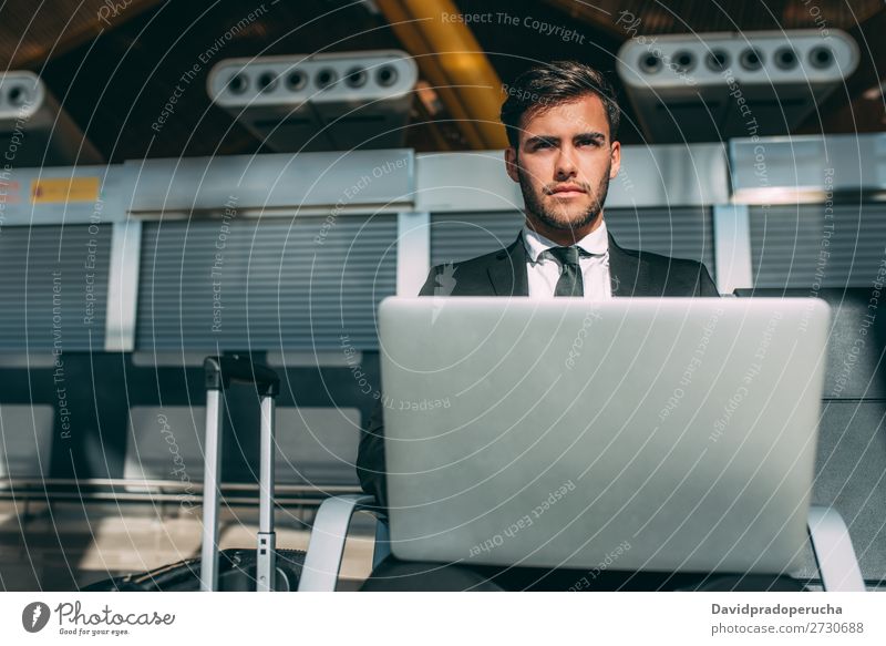 Junger Geschäftsmann sitzt am Computer mit dem Koffer am Flughafen und wartet auf den Flug. Mann Ferien & Urlaub & Reisen Notebook WiFi Technik & Technologie