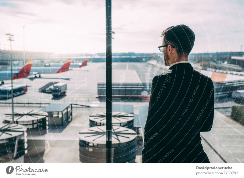 Zurück von einem jungen Geschäftsmann, der mit dem Koffer am Flughafen steht und auf den Flug wartet. Mann Ferien & Urlaub & Reisen Schatten Rücken Business