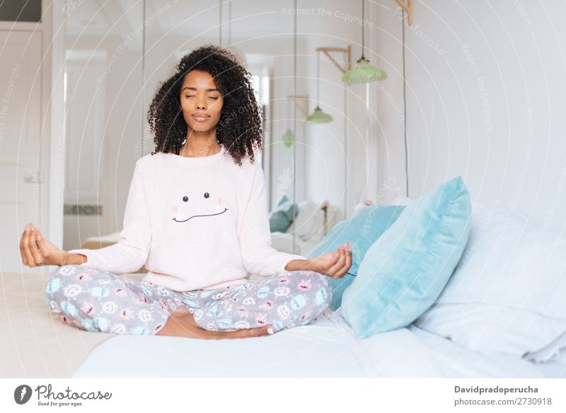 Glückliche, schöne, junge, schwarze Frau, die sich zu Hause entspannt und die Morgenmeditation im Bett macht. Yoga Meditation Verstand Schlafanzug Pyjama üben