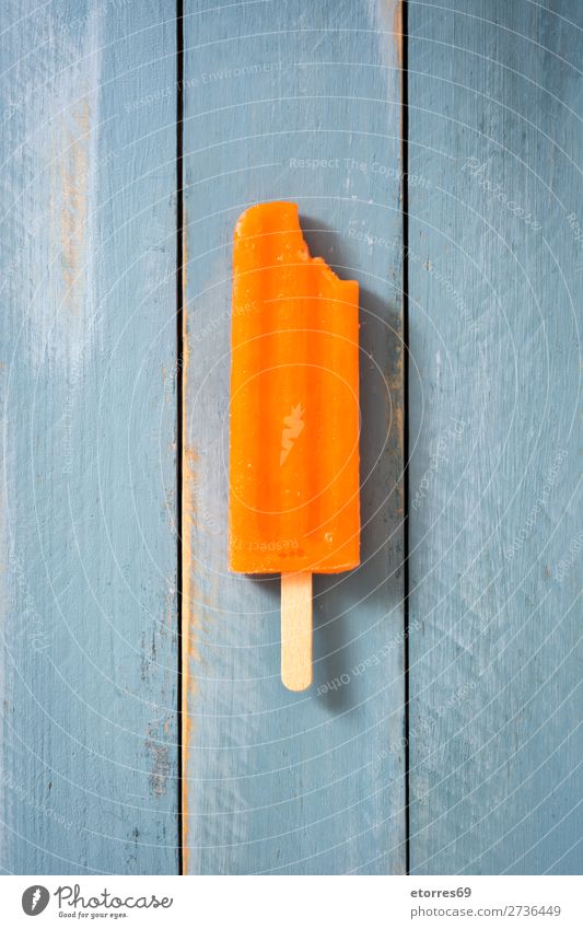 Oranges Stieleis auf blauem Holztisch. Draufsicht Backwaren orange Sommer Eis Speiseeis kalt Lebensmittel Gesunde Ernährung Foodfotografie Dessert gefroren