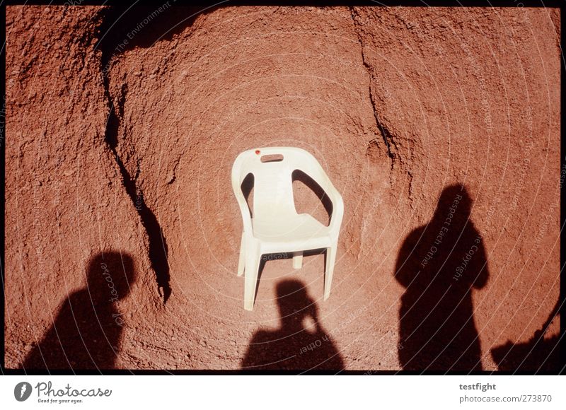 a chair Mensch 3 Erde Sand skurril Kot Plastikstuhl Gartenstuhl Felsen rot Schatten Schattenspiel Farbfoto Außenaufnahme Detailaufnahme abstrakt Tag Sonnenlicht