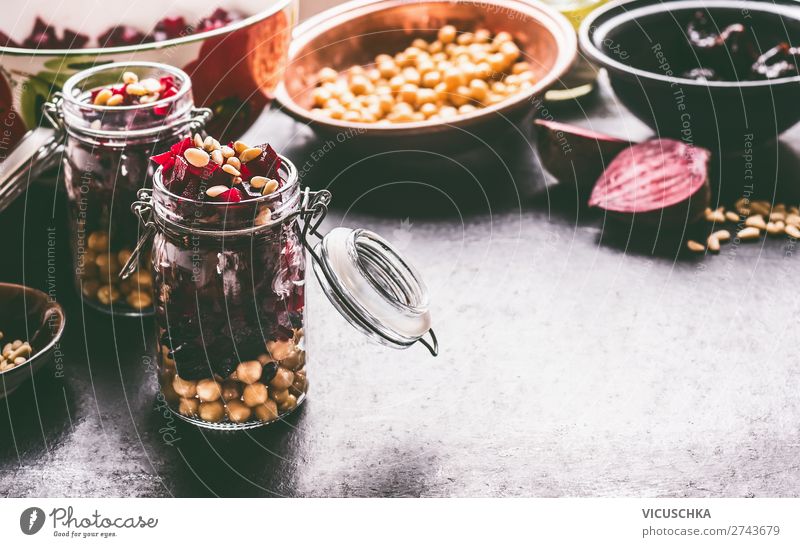 Gesunder hausgemachter Rote-Bete-Salat mit Kichererbsen und Pinienkernen in Gläsern zum Mittagessen auf dunklem Küchentischhintergrund mit Zutaten, Ansicht von oben. Violettes Gemüse essen. Saubere Diätnahrung.