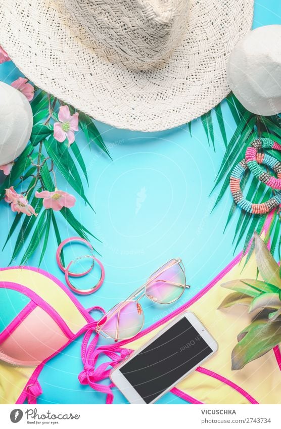 Draufsicht auf weibliche Strandaccessoires im Hintergrund mit tropischen Blättern und Blumen, Sonnenbrille und Strohhut, Bikini und Smartphone auf Sonnenblau. Konzept für den Sommerurlaub