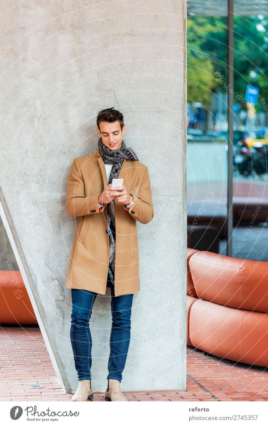 junger Mann in Jeanskleidung, der sich an eine Wand lehnt, während er im Freien ein Mobiltelefon benutzt Lifestyle elegant Stil schön Haare & Frisuren Telefon