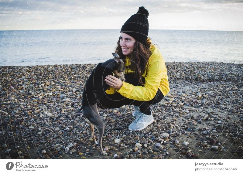 Frau mit ihrem kleinen Hund am Strand Lifestyle Erholung Ausflug Freiheit Sonne Winter Freundschaft 30-45 Jahre Erwachsene Natur Tier Horizont Küste Jacke