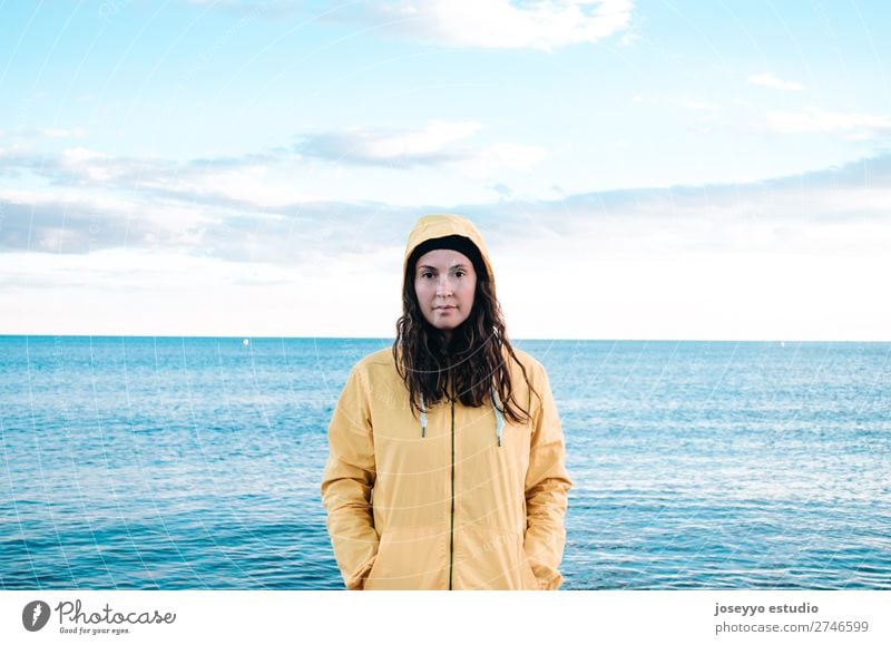 Frau am Strand mit gelbem Regenmantel und Hut Lifestyle Leben Erholung Ausflug Freiheit Sonne Winter Sport Sitzung 30-45 Jahre Erwachsene Natur Horizont Küste