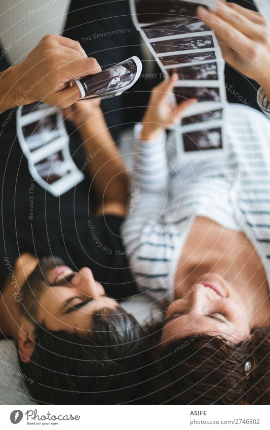 Ein glückliches und aufgeregtes schwangeres Paar, das sich die Ultraschallbilder seines auf dem Bett liegenden Babys ansieht Glück schön Leben Frau Erwachsene