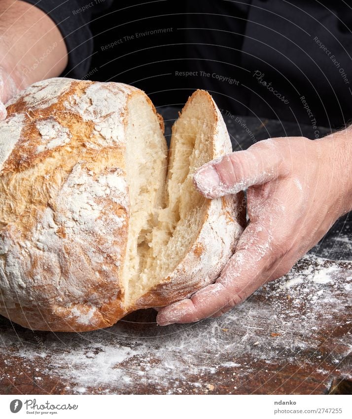 Koch in einer schwarzen Tunika hält frisch gebackenes Brot bereit. Ernährung Frühstück Tisch Küche Mensch Hand Finger Holz machen dunkel braun weiß Tradition