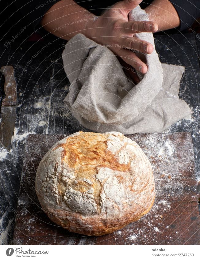 gebackenes Rundbrot auf einem Brett Brot Ernährung Tisch Küche Beruf Koch Mensch Hand Finger Holz machen dunkel frisch braun schwarz weiß Tradition Küchenchef