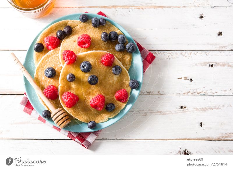 Pfannkuchen mit Himbeeren, Heidelbeeren und Honig süß Dessert Frühstück Blaubeeren Beeren blau rot backen Lebensmittel Speise Foodfotografie Teller vereinzelt