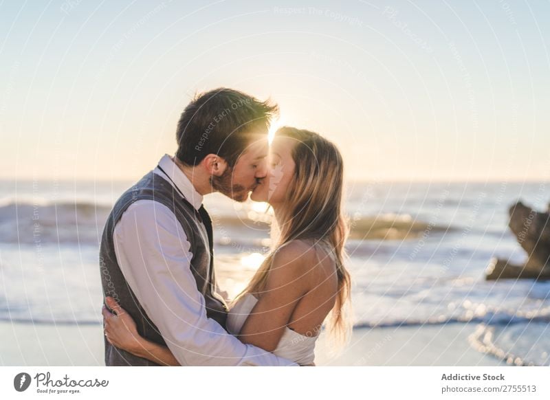 Zärtlich küssendes Brautpaar im Sonnenlicht Paar Hochzeit Strand umarmend Engagement Zufriedenheit Valentinsgruß Genuss verliebt Meereslandschaft stehen