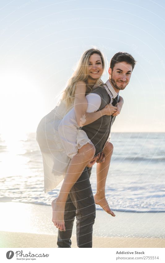 Bräutigam mit charmantem Mädchen auf dem Rücken Paar Hochzeit auf der Rückseite Strand Sommer Meer striegeln verliebt Braut tragen Erholung lachen heiter Kleid