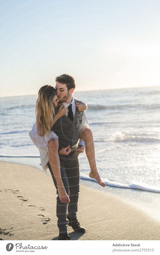 Bräutigam mit charmantem Mädchen auf dem Rücken Paar Hochzeit auf der Rückseite Strand Sommer Meer striegeln verliebt Braut tragen Erholung heiter Kleid schön