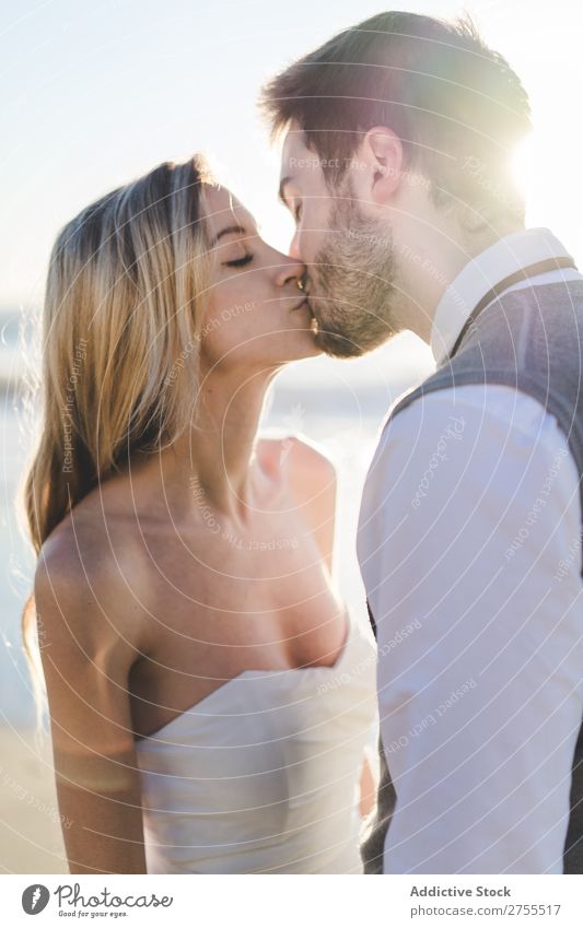 Zärtlich küssendes Brautpaar im Sonnenlicht Paar Hochzeit Strand umarmend Engagement Zufriedenheit Valentinsgruß Genuss verliebt Meereslandschaft stehen