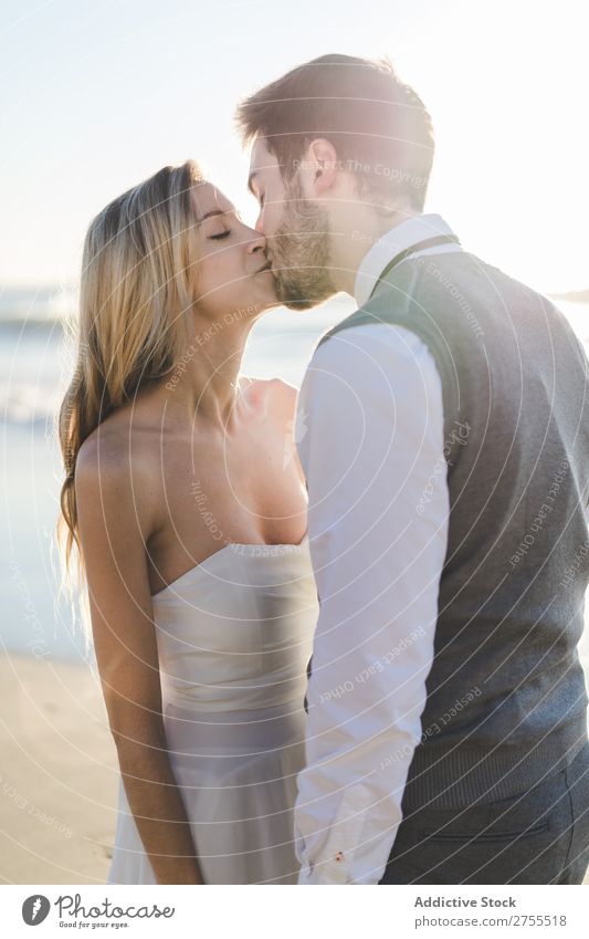 Zärtlich küssendes Brautpaar im Sonnenlicht Paar Hochzeit Strand umarmend Engagement Zufriedenheit Valentinsgruß Genuss verliebt Meereslandschaft stehen