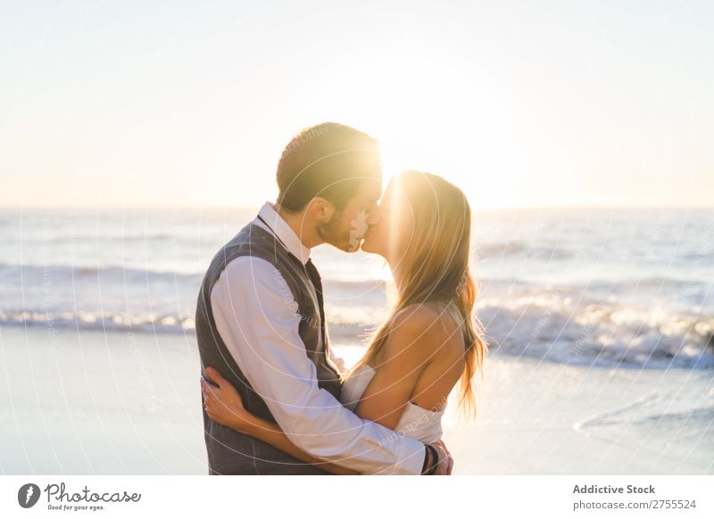 Zärtlich küssendes Brautpaar im Sonnenlicht Paar Hochzeit Strand umarmend Engagement Zufriedenheit Valentinsgruß Genuss verliebt Meereslandschaft stehen