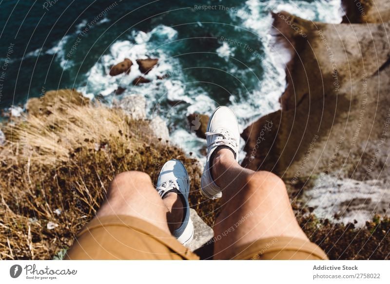 Mann sitzt auf einer Klippe. Ferien & Urlaub & Reisen Beine Lifestyle Mensch Erwachsene Stein Felsen Natur Abenteuer Freiheit Reisender Ausflug Tourist heiß