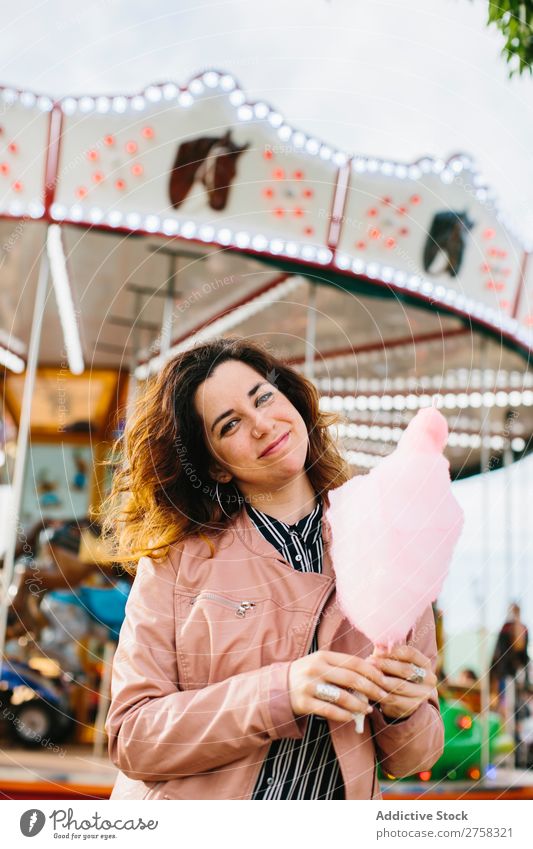 Lächelnde Frau hält eine Zuckerwatte in der Nähe des Karussells. Park Kinderkarussell Person rosa hübsch süß Lebensmittel essen Spaß Lifestyle Porträt jung