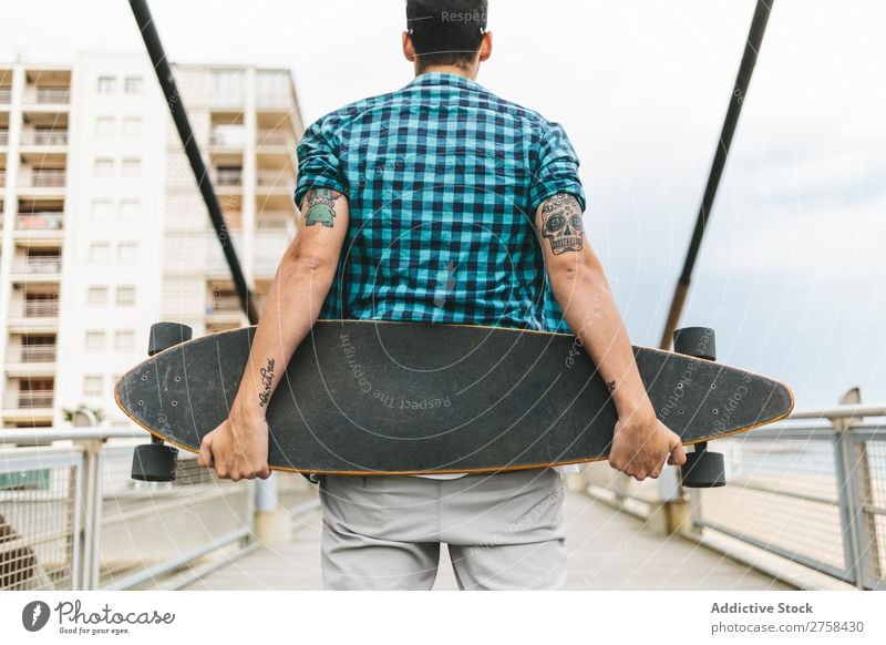 Mann mit Tattoos, der Skateboard an Land hält. Rückansicht. Küste Strand Freizeit & Hobby Sommer mehrfarbig Youngster Aktion Jugendliche Sport Schlittschuhe