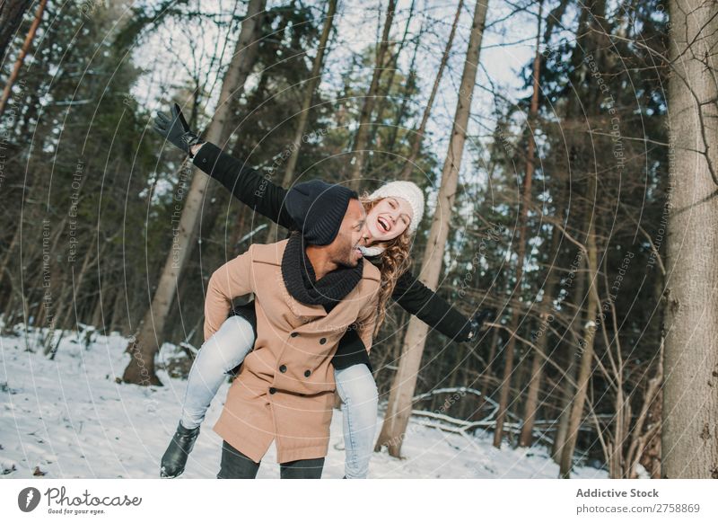 Ein Paar mit Spaß im Winterwald multiethnisch Stil warme Kleidung lässig Natur Wald Schnee Huckepack schön Person gemischter Abstammung schwarz Jugendliche