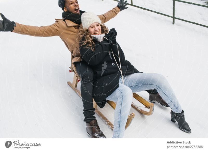 Ein paar Schlittenfahrten auf einem schneebedeckten Hügel Paar multiethnisch Stil warme Kleidung lässig Natur Rodel Reiten Winter Schnee schön