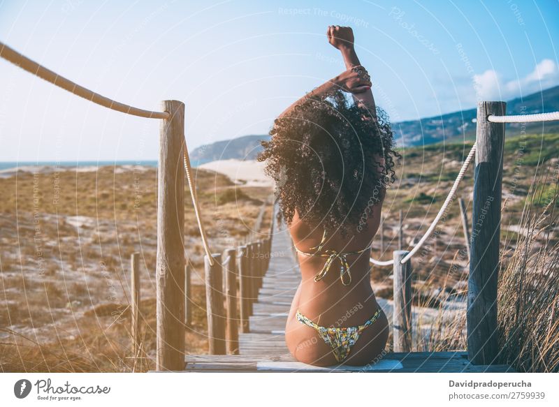 Schöne junge schwarze Frau, die in einer hölzernen Fußgängerbrücke am Strand sitzt. Hintergrundbild Bikini Brücke Küste krause Haare Ausflugsziel Behaarung