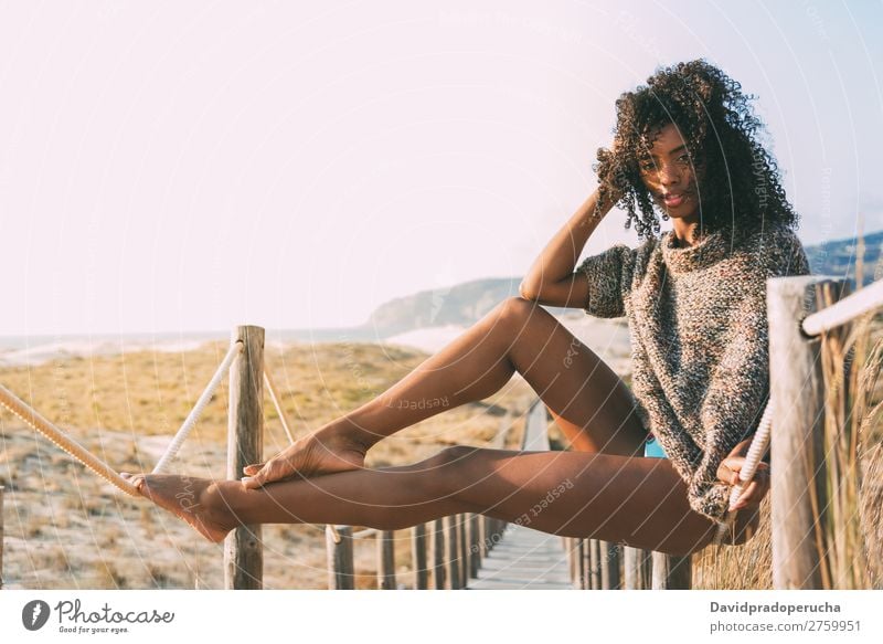 Schöne junge schwarze Frau, die in einer hölzernen Fußgängerbrücke am Strand sitzt. Hintergrundbild Bikini Brücke Küste krause Haare Ausflugsziel Behaarung