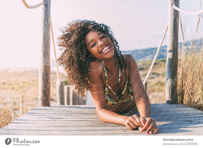 Schöne junge schwarze Frau, die in einer hölzernen Fußgängerbrücke am Strand liegt. Hintergrundbild Bikini Brücke Küste krause Haare Ausflugsziel Mädchen