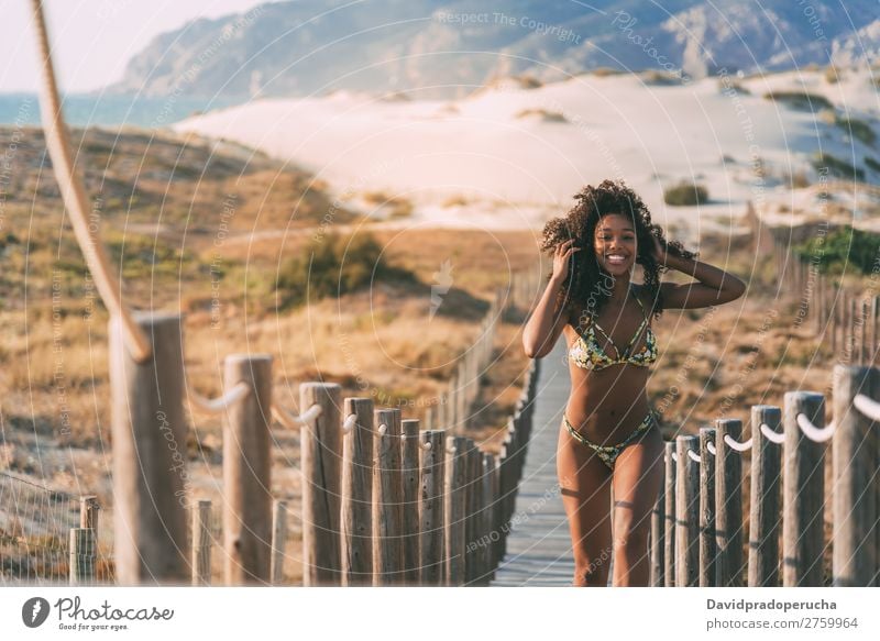 Schöne junge Frau im Bikini, die in einer Holzsteg am Strand läuft. schwarz Brücke Hintergrundbild Küste krause Haare Ausflugsziel Mädchen niedlich hübsch schön