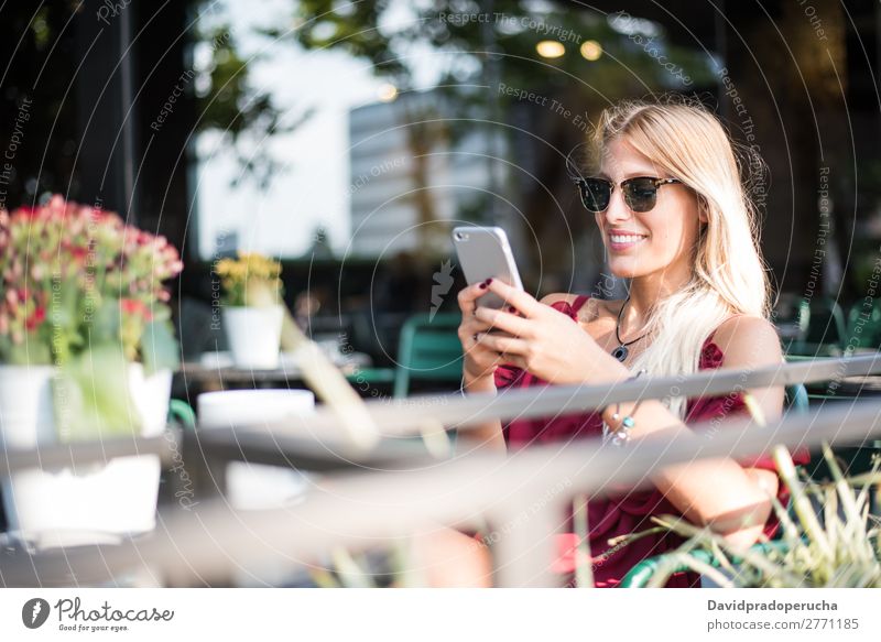 Glückliche blonde schöne Frau mit einem Handy, die eine Tasse Kaffee auf der Terrasse trinkt. Lächeln PDA Sonnenbrille Restaurant Kantine Schüler vereinzelt