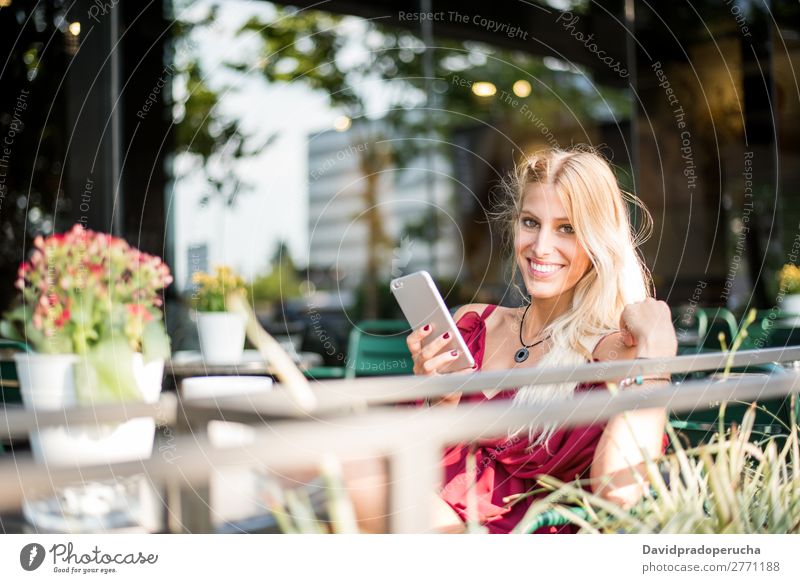 Glückliche blonde schöne Frau mit einem Handy, die eine Tasse Kaffee auf der Terrasse trinkt. Lächeln PDA Sonnenbrille Restaurant Kantine Schüler vereinzelt